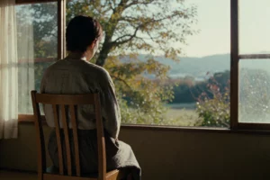 A contemplative scene from the film 'Оглянись' (After Life) by Hirokazu Kore-eda, showing a quiet, softly lit room with a single wooden chair facing a large window that frames a serene natural landscape — trees, soft sunlight, and distant hills. A person sits in the chair, seen from behind, wearing simple, modest clothing, lost in thought. The atmosphere is peaceful, introspective, and emotionally resonant, reflecting the film’s themes of memory and choice. No text, signs, or modern objects visi