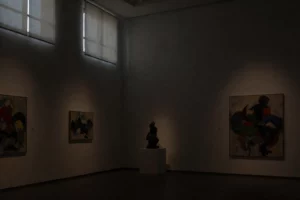 A dimly lit art gallery interior with soft, barely visible light filtering through high windows, casting faint shadows on minimalist white walls displaying abstract paintings; a single spotlight barely illuminates a sculpture in the center, creating an atmosphere of quiet contemplation and near-darkness, with subtle details visible only upon close inspection